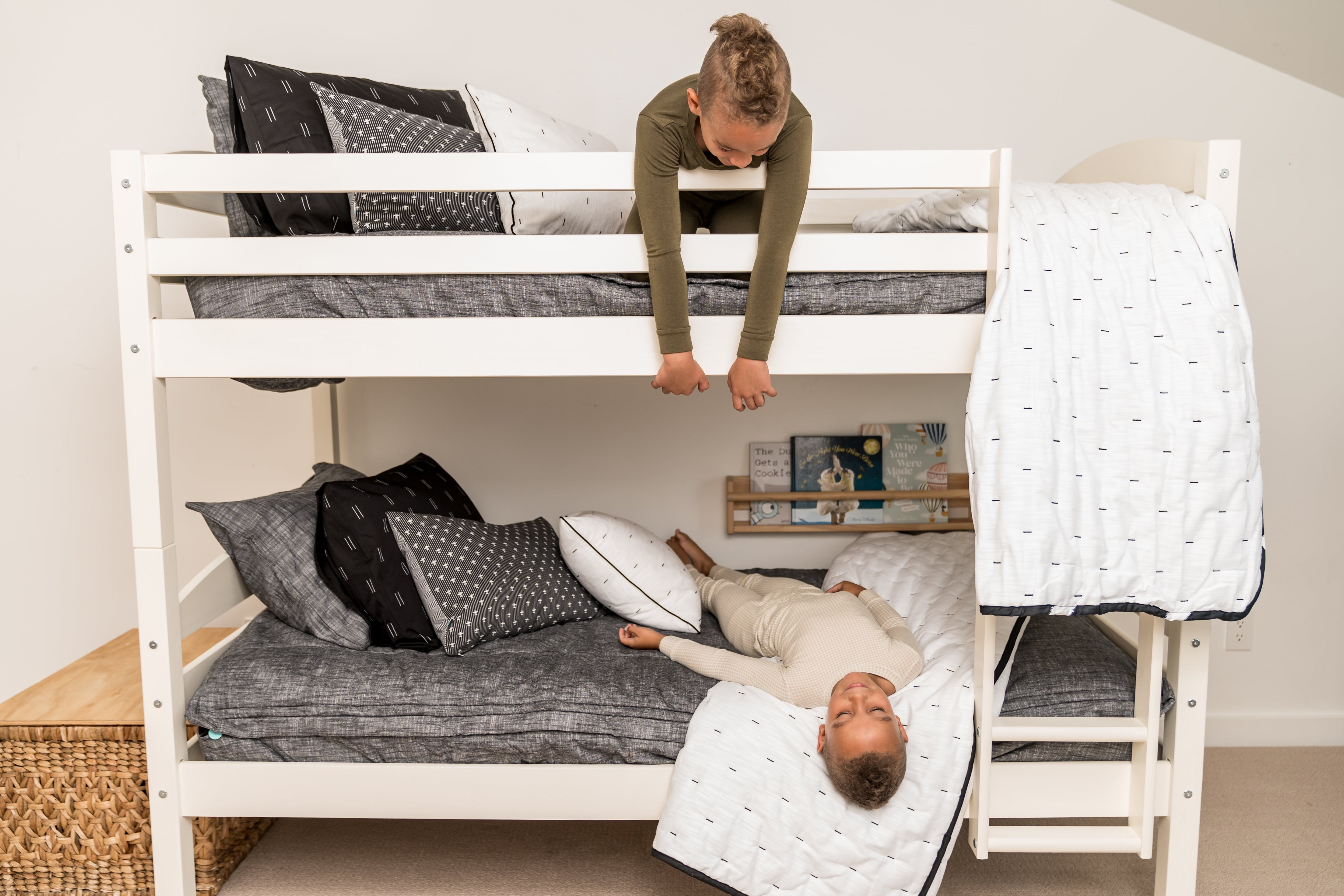 A bunk bed where both beds are made with gray zipper bedding, a boy on the top bunk looking down at his brother who is laying on the bottom bunk.