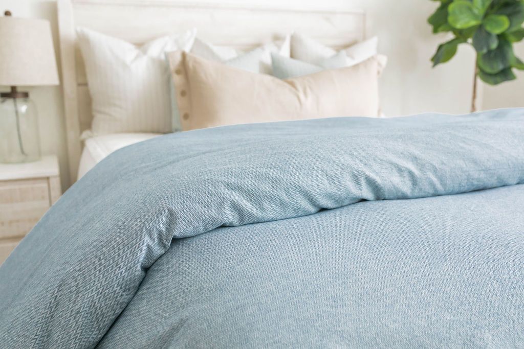 A side shot of a bed made with white zipper bedding and a chambray blue duvet.