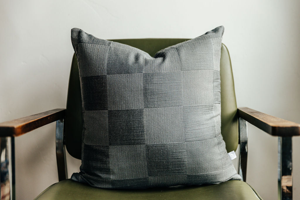 A two toned gray pillow with a checkerboard pattern sitting on a green chair.