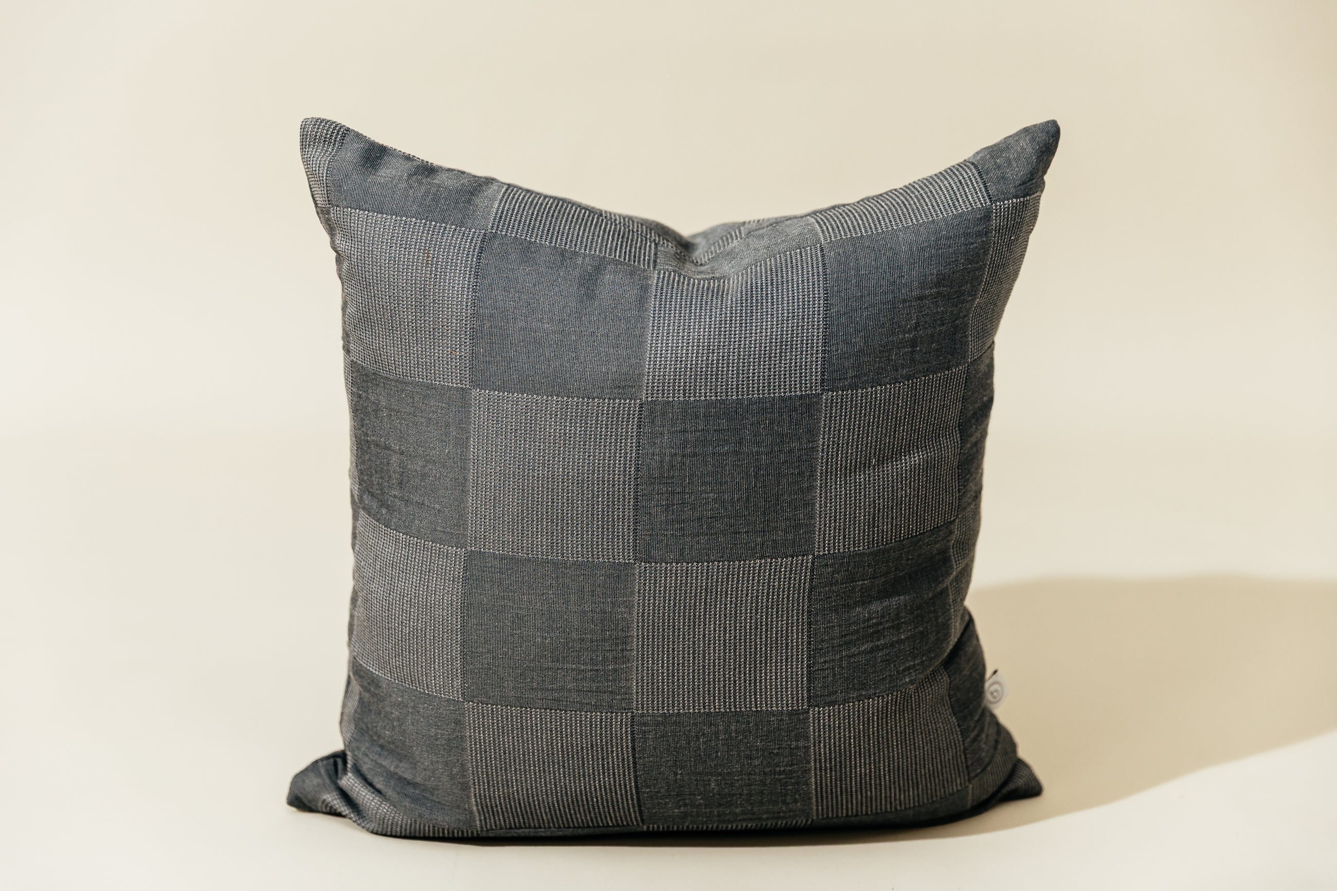 A checkerboard two toned gray pillow on a cream backdrop.