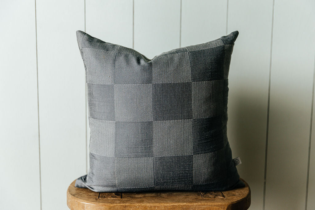 A checkerboard two toned gray pillow sitting on a stool