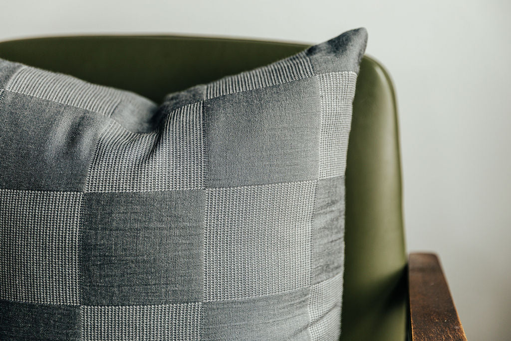 A close up on a checkerboard two toned gray pillow sitting on a green chair.