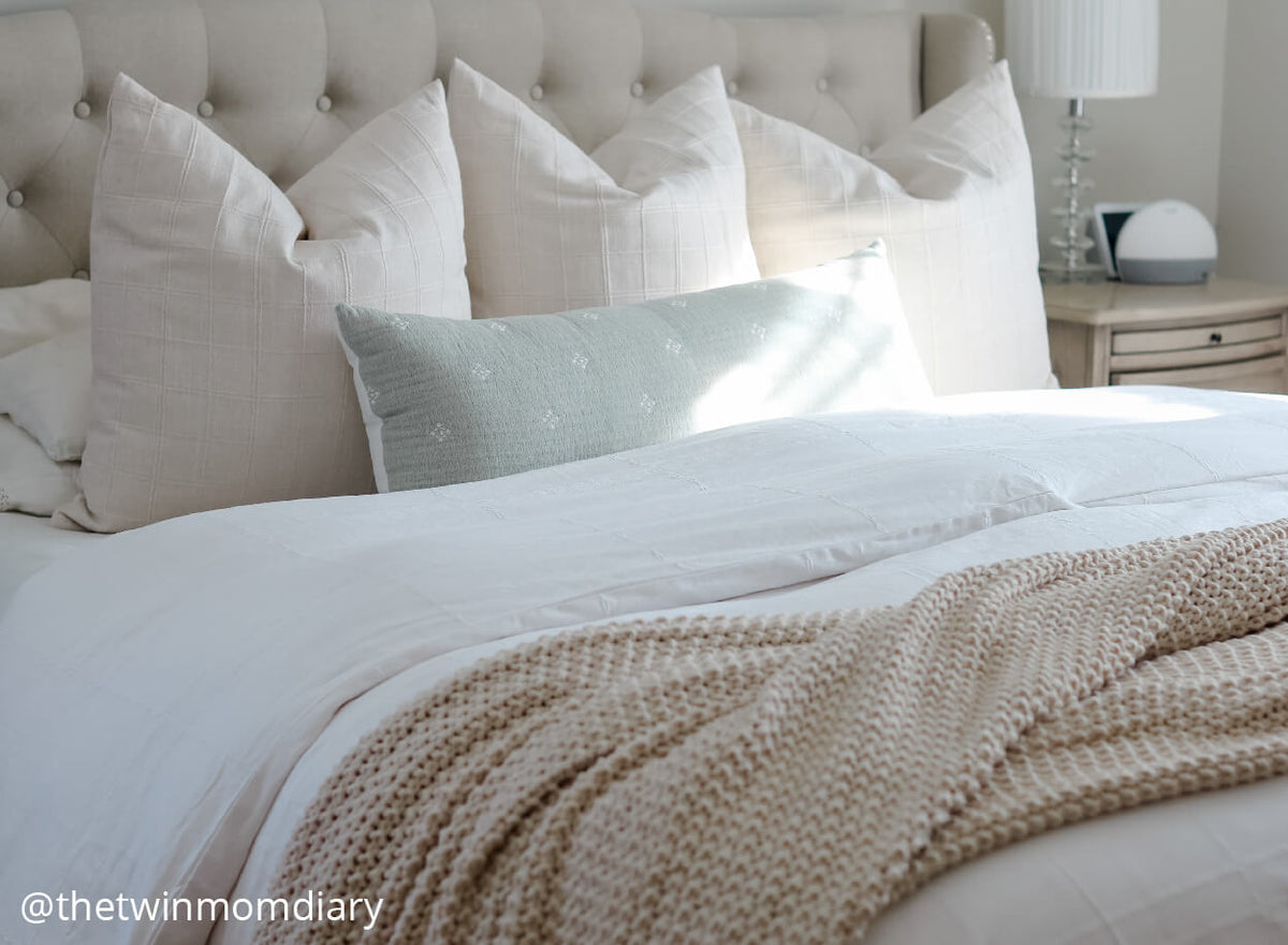 A queen bed made with a white duvet, a waffle knit throw across the foot of the bed and neutral colored and blue pillows arranged on top.