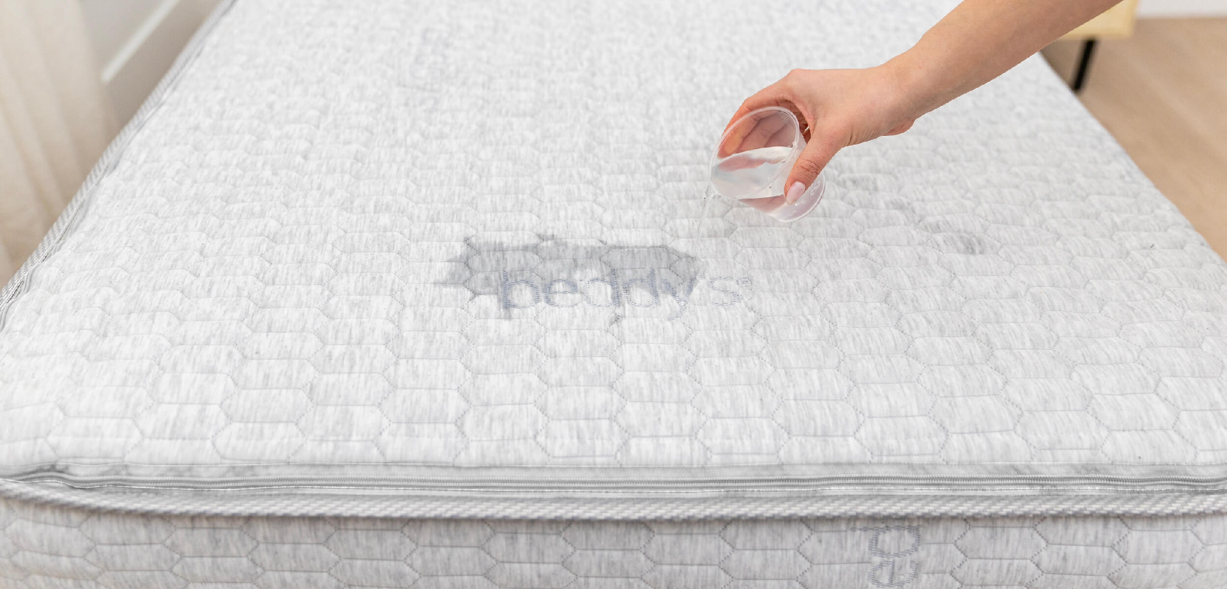 The Beddy's ZipClean Mattress with someone pouring a small cup of water over the top to show that it is moisture resistant.