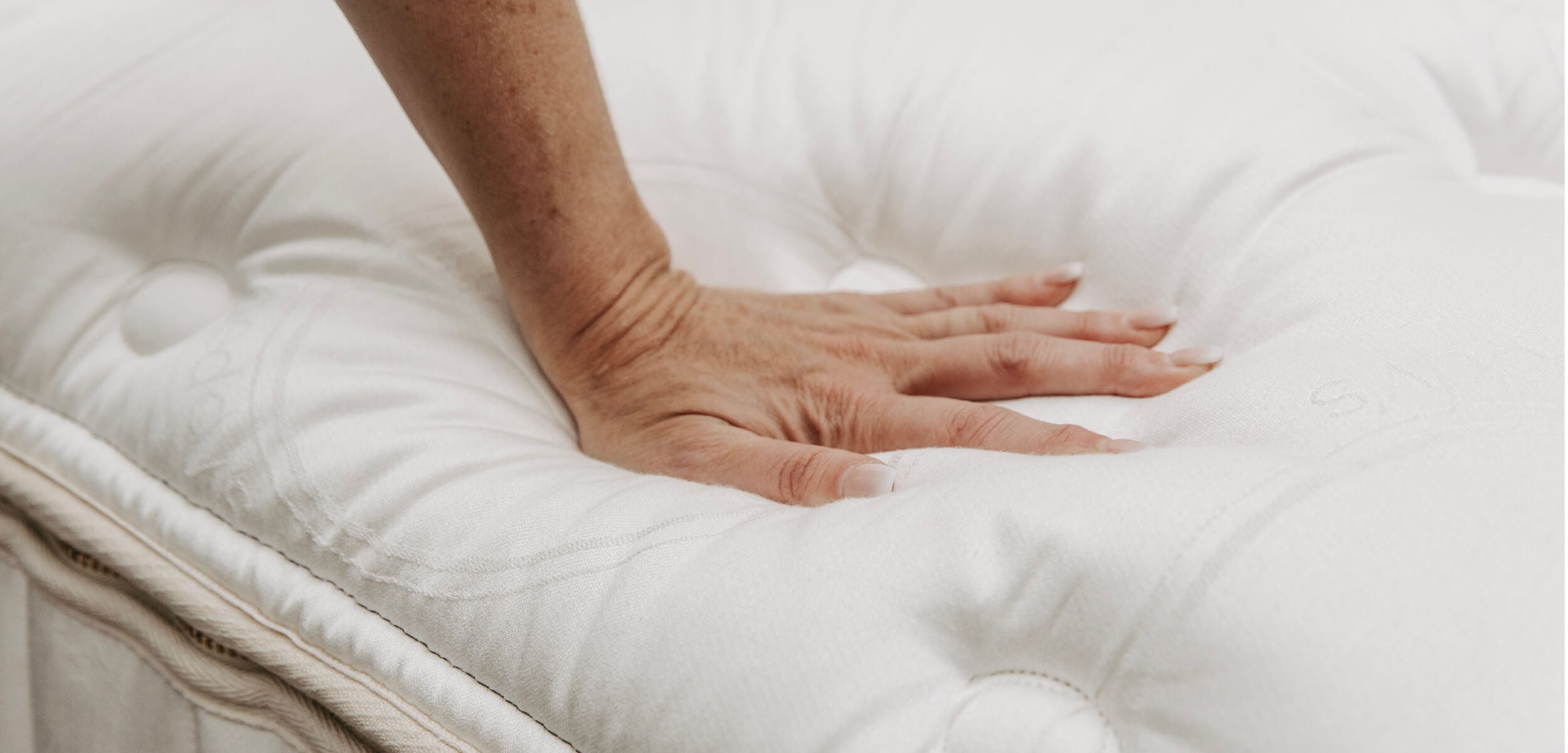 A hand pressing. down on the tufted, luxurious top layer of the Beddy's ZipLuxe Mattress to help demonstrate how plush and comfortable it is.