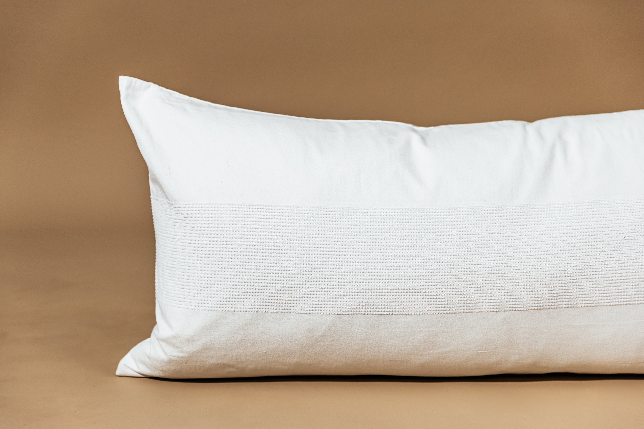 A white lumbar pillow on a brown backdrop.