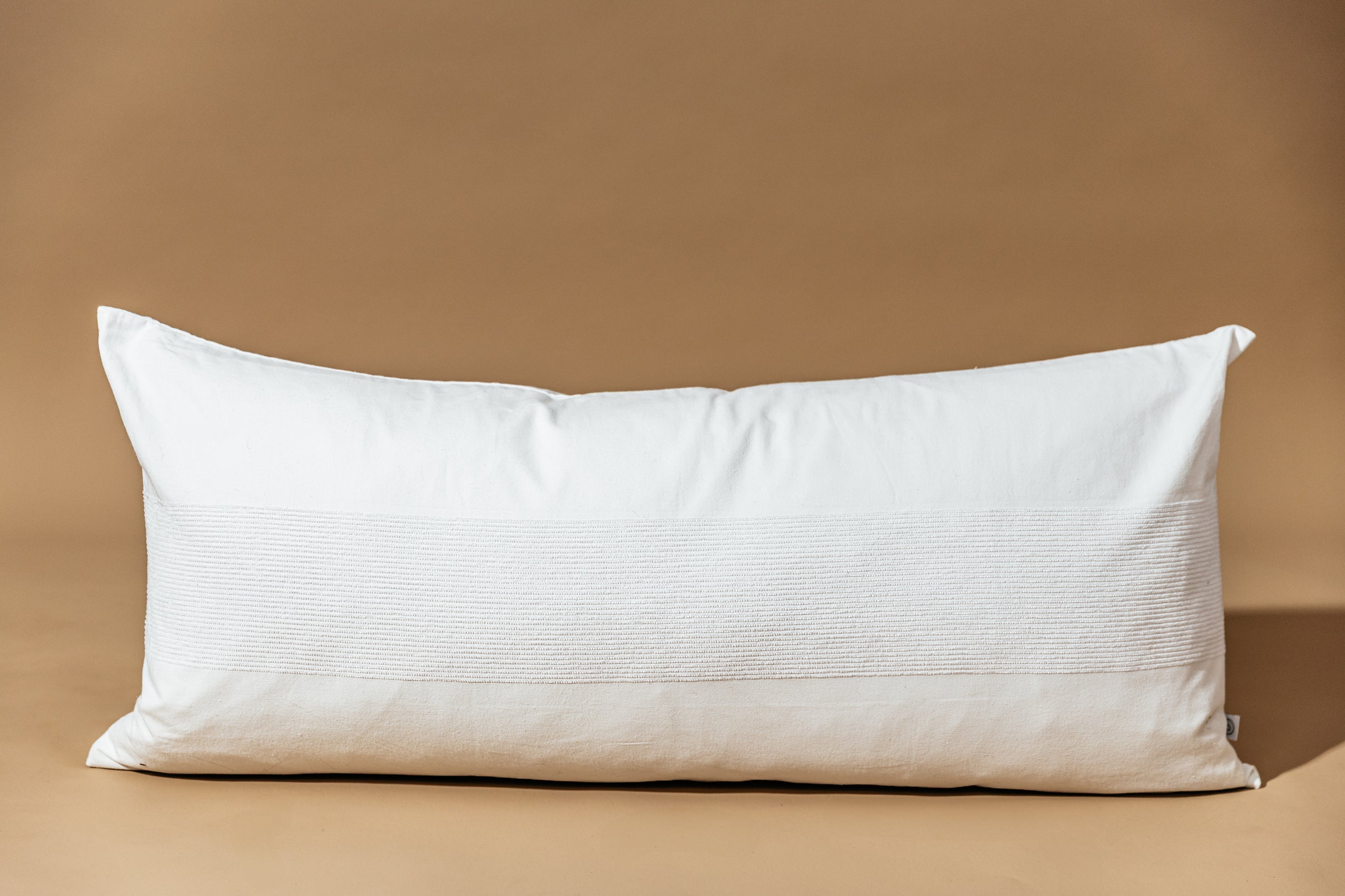 A white lumbar pillow on a brown backdrop.