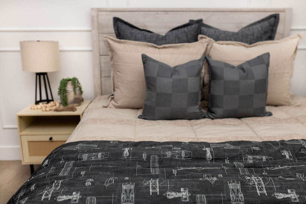 A bed made with tan zipper bedding and an assortment of neutral and black throw pillows and blanket.