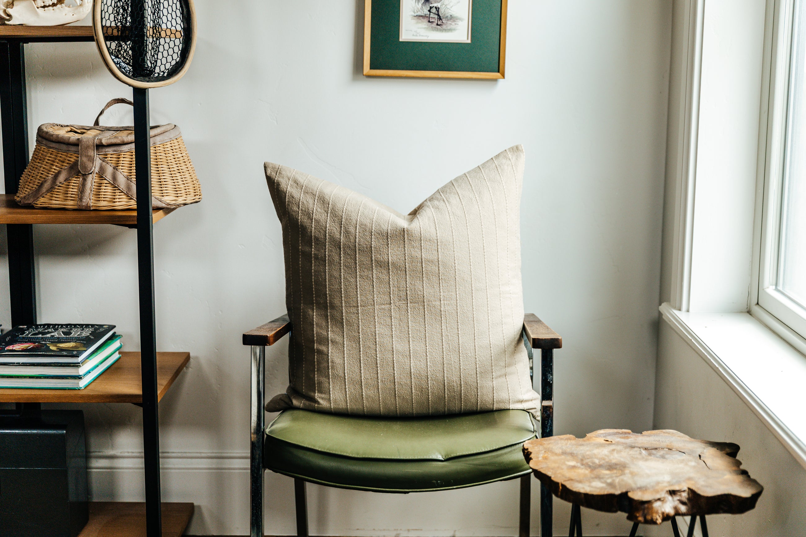 A neutral striped euro sham sitting on a green chair in the corner of a living room.
