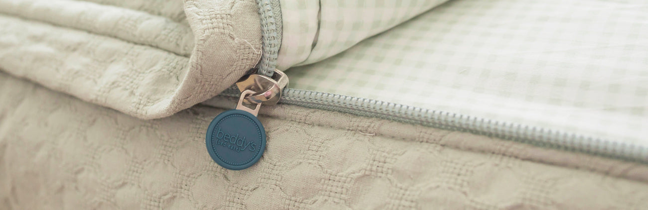 A close up shot of a zipper on a sage green zipper bedding set, the bed slightly unzipped.