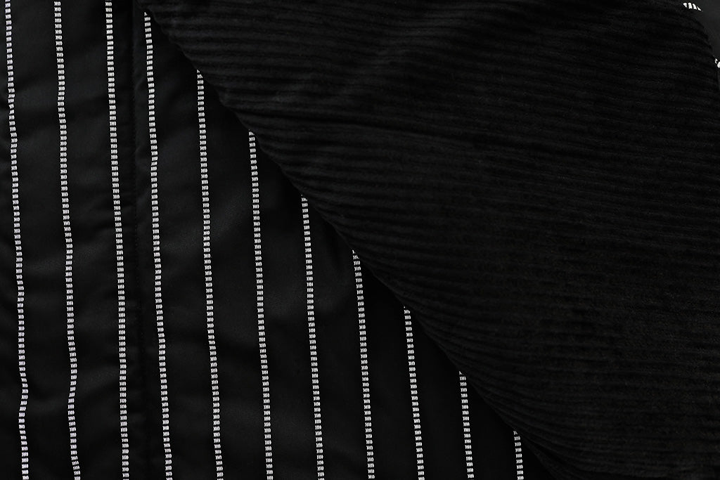A close up of a black striped blanket with one side folded over to reveal the minky side.