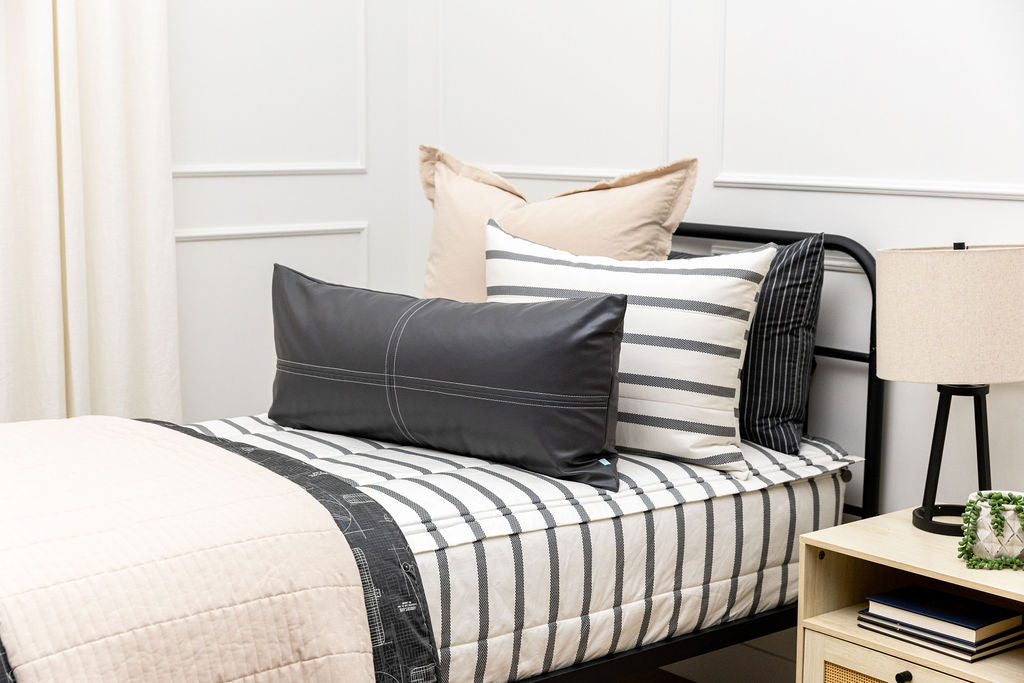 A twin bed made with white and black striped zipper bedding paired with neutral tan and black accessories.