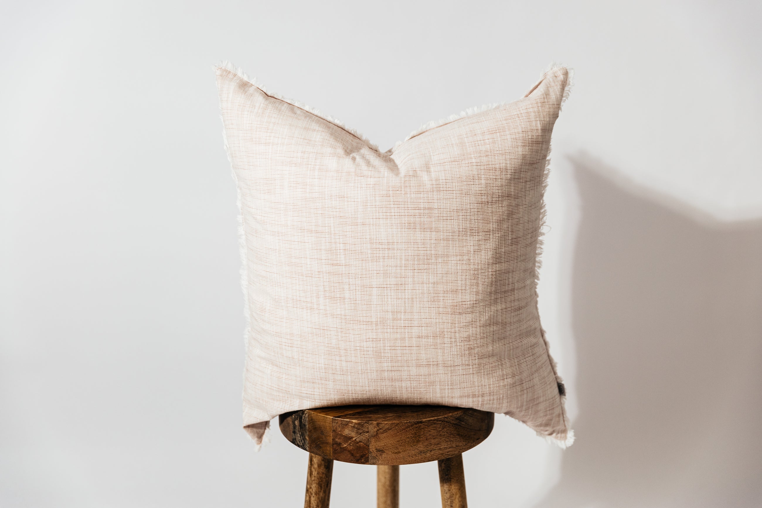 A light pink woven striped euro pillow arranged on a wood stool with a white background.
