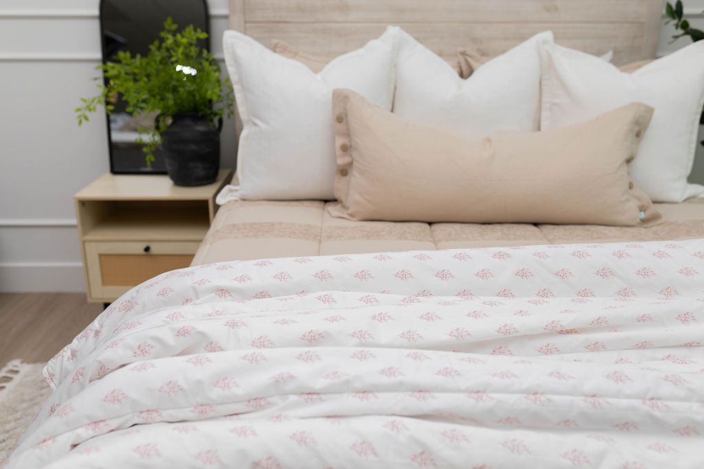 A close up of a bed made with tan striped zipper bedding and neutral pillows with a pink floral pattern white blanket at the end of the bed.