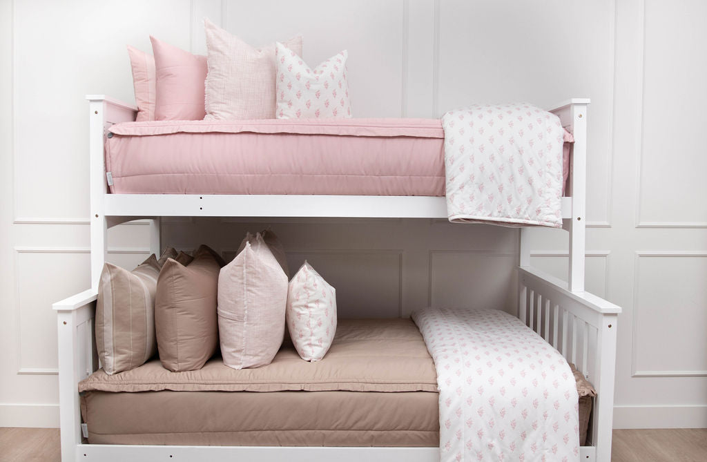 A standard bunk bed with both bunks made with zipper bedding, one with pink and one with tan as well as matching floral pink pillows and blankets.