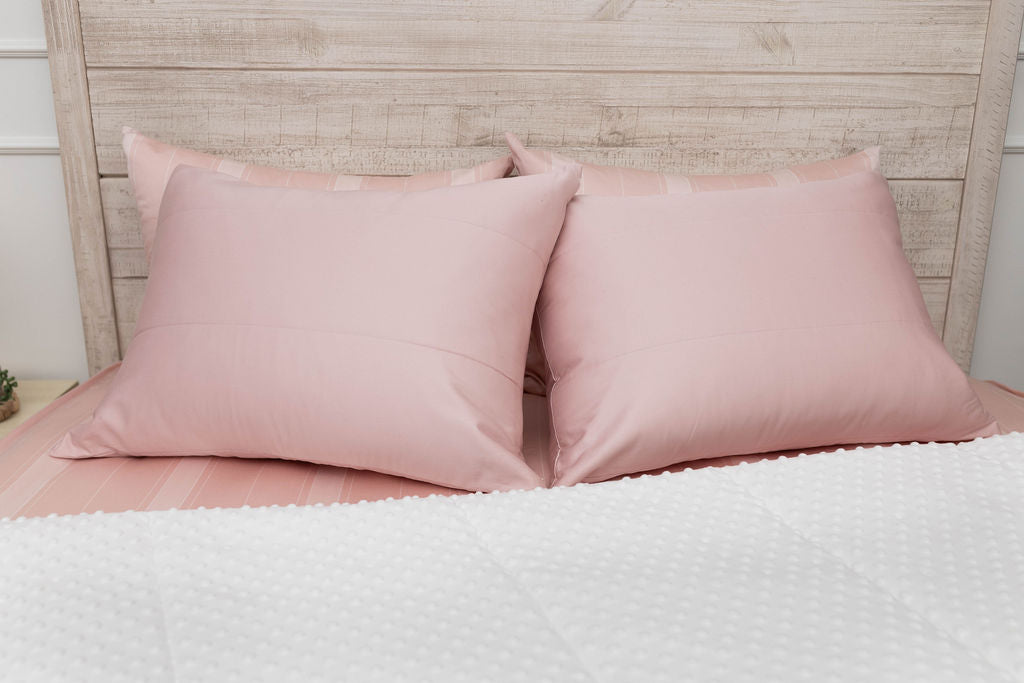 A bed made with pink zipper bedding with the comforter pulled back showing minky interior lining and pillows on top of the bed.