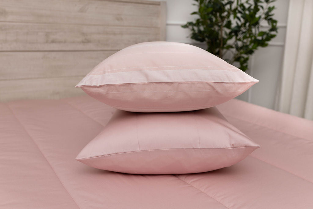 A pink striped pillowcase and matching sham on a made bed with pink zipper bedding.