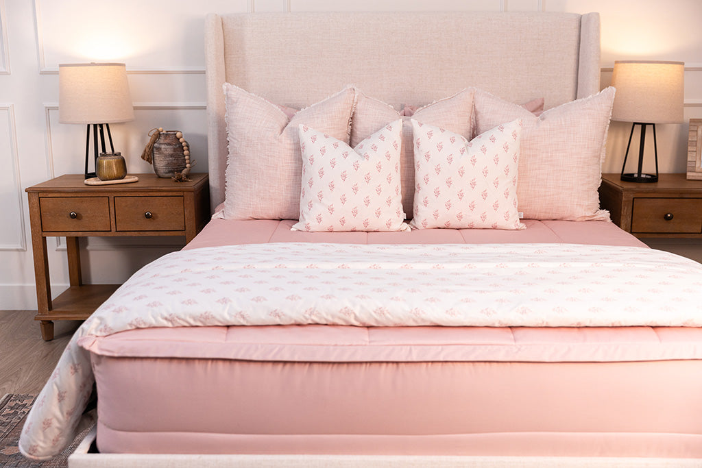 A bed made with pink zipper bedding and an assortment of light pink and floral pillows and blanket.