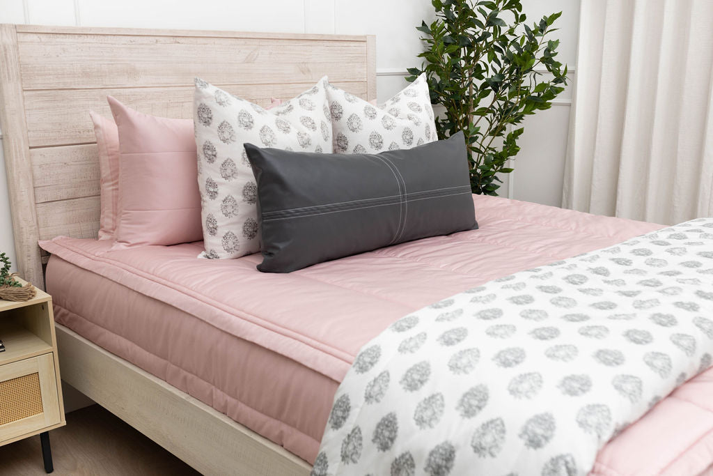 A bed made with pink zipper bedding and an assortment of leather and gray pattern pillows and blanket.
