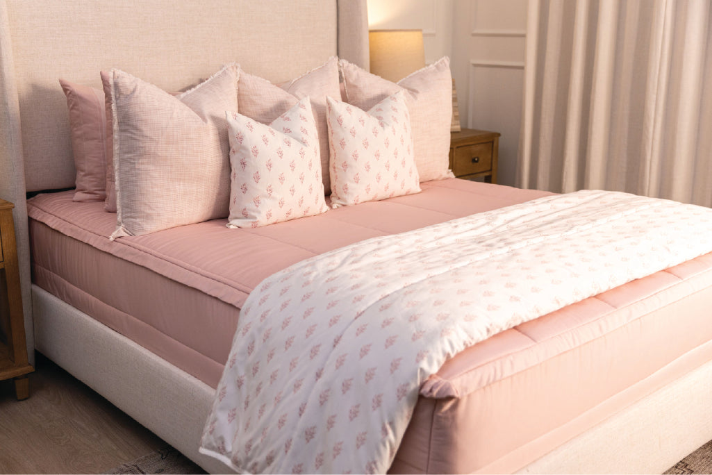 A bed made with pink zipper bedding and an assortment of light pink and floral pillows and blanket.