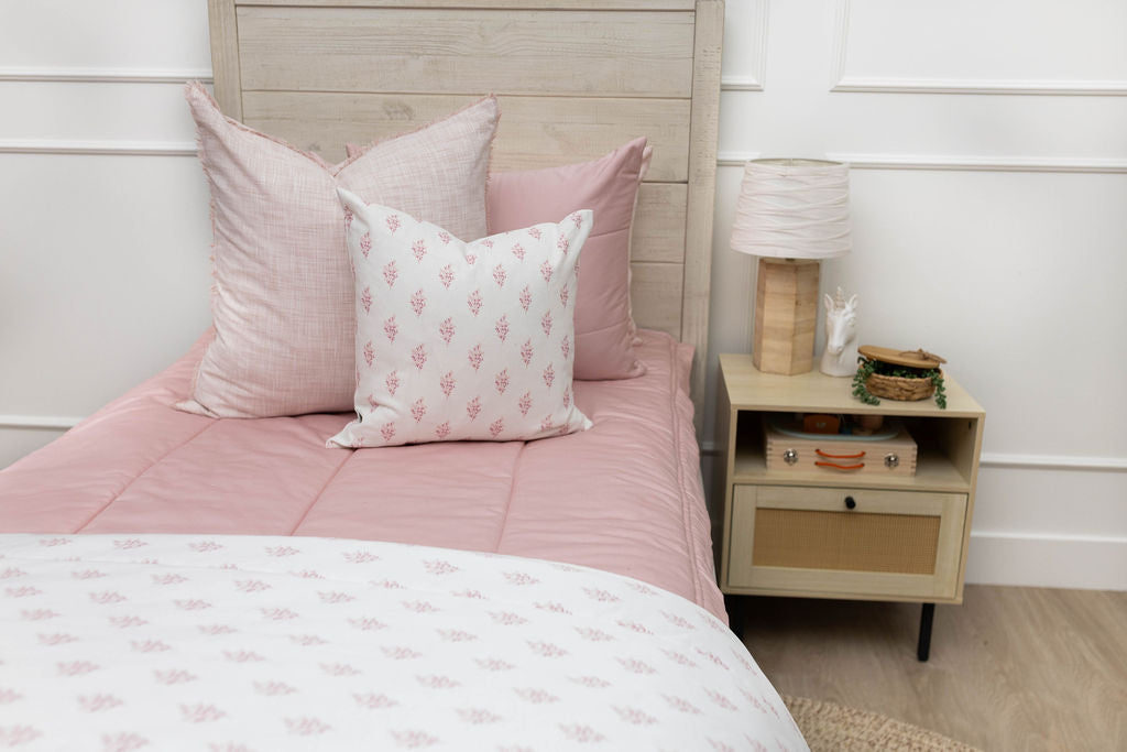 A twin bed made with pink zipper bedding and light pink and floral pillows and blanket.