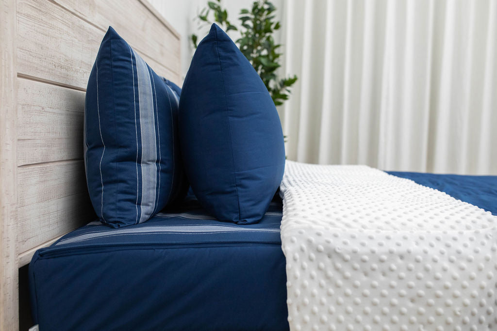 A side view of a bed made with navy zipper bedding with the top unzipped halfway down the bed and the comforter folded down.