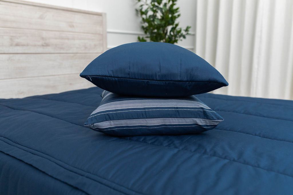 A navy blue zipper bedding made with the matching pillows stacked in the middle of the bed.