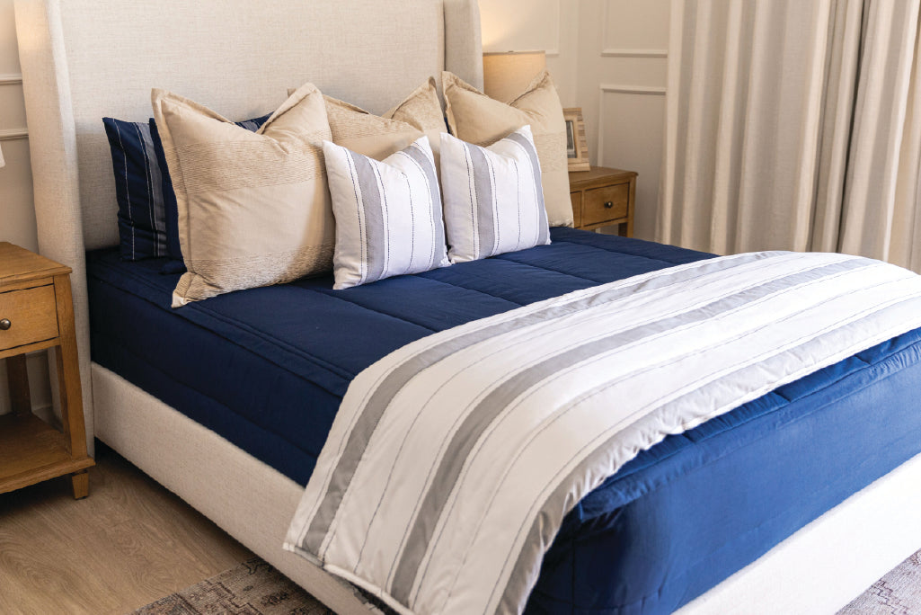 A bed made with navy blue zipper bedding and an assortment of neutral and striped throw pillows and blanket.