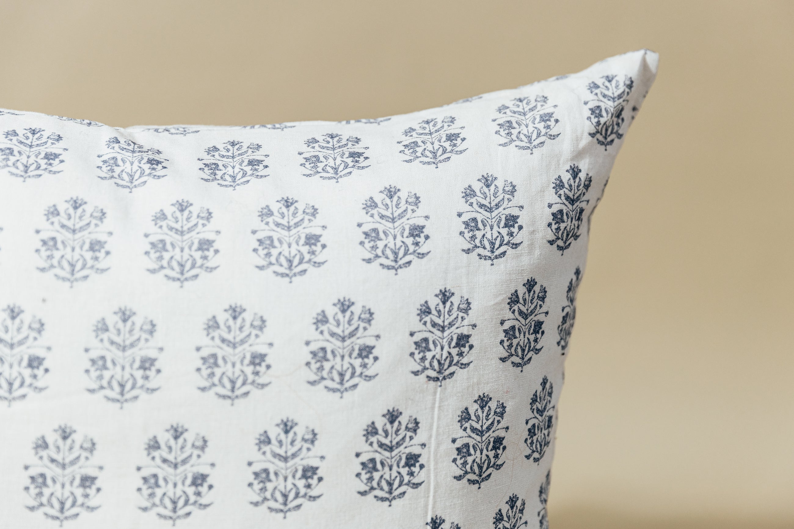 A close up corner view of a white euro pillow with a blue floral design arranged on a tan background.