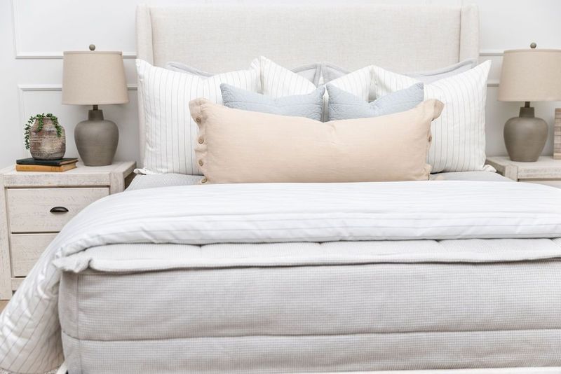 A bed made with light gray waffle texture zipper bedding and an assortment of neutral and striped pillows and blanket.