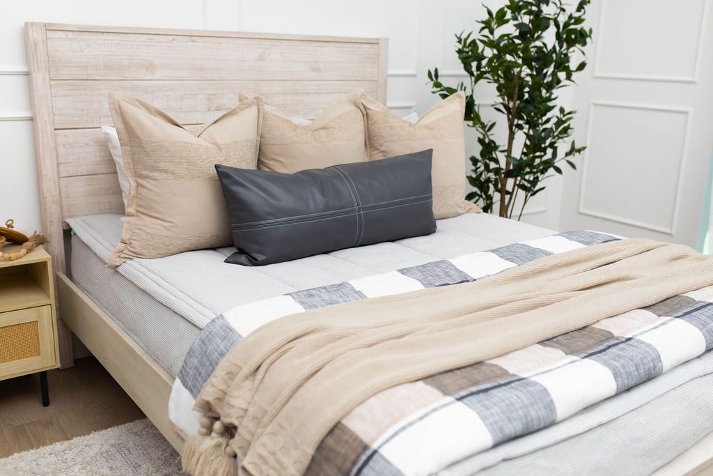 A bed made with light gray waffle textured zipper bedding and an assortment of tan and neutral throw pillows and blankets.
