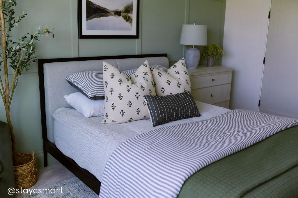 A bed made with light gray waffled textured zipper bedding and an assortment of green and neutral patterned pillows and blankets.