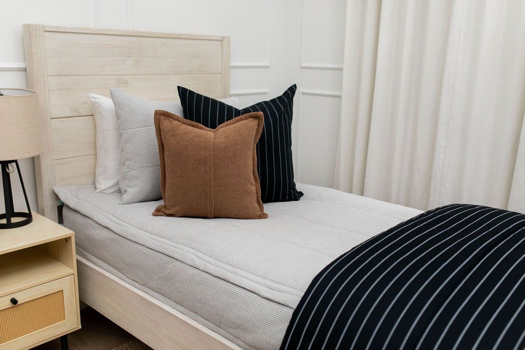 A twin bed made with light gray waffle textured zipper bedding and an assortment of black striped and neutral pillows and blanket.