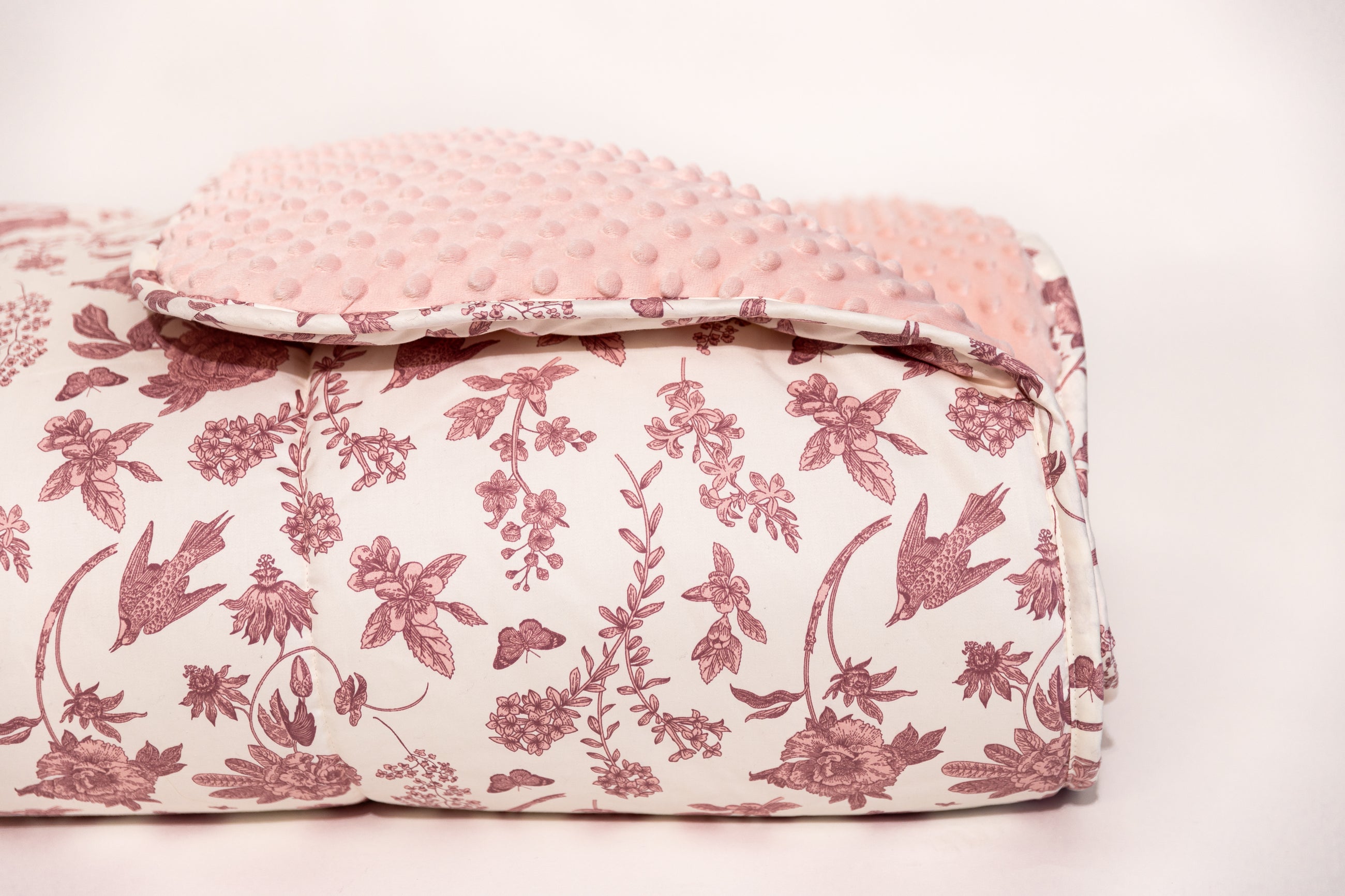 Pink and white floral blanket with folded corner showing pink minky