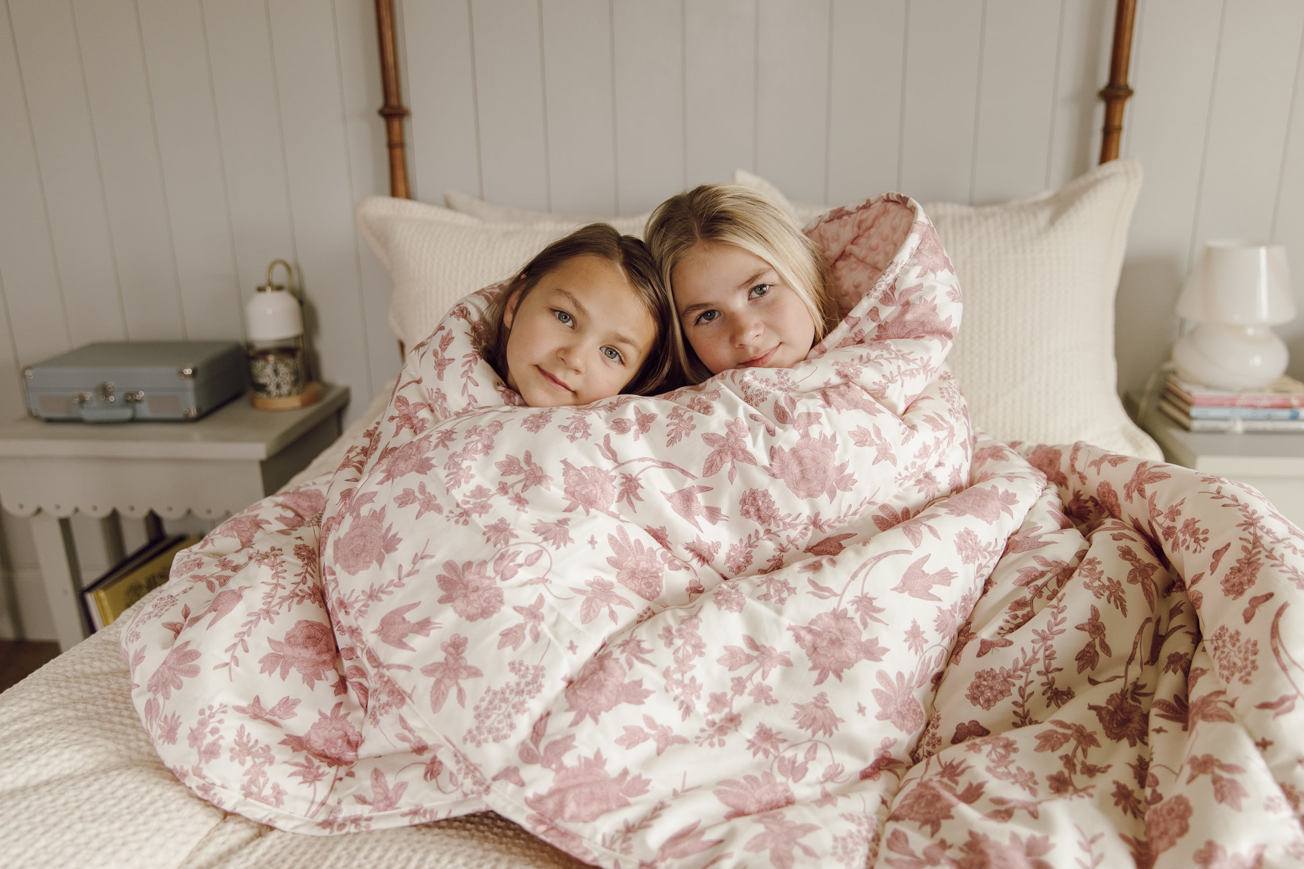 Two girls wrapped in pink and white floral blanket on bed