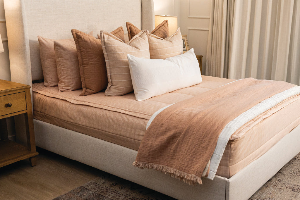 A Queen bed made with peachy pink zipper bedding and an assortment of pink and terra cotta bedding accessories