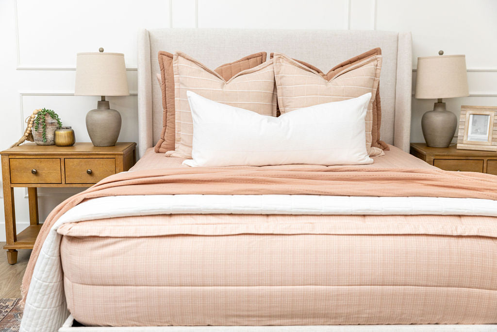 A queen bed made with peach pink zipper bedding adorned with neutral and pink pillows and blankets.