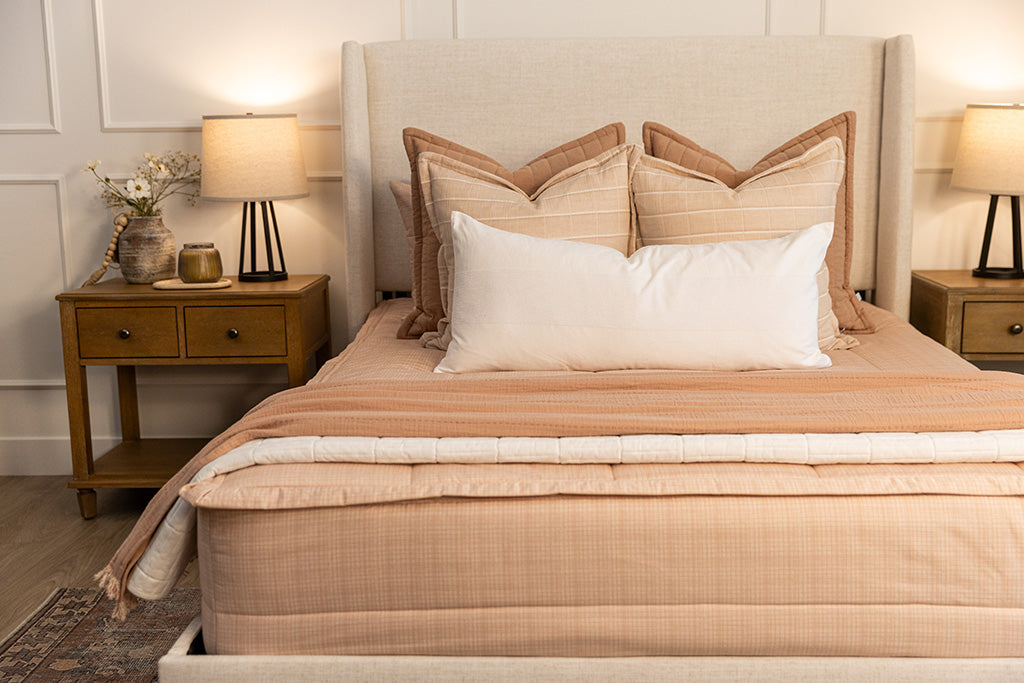 A queen bed made with peach pink zipper bedding adorned with neutral and pink pillows and blankets.