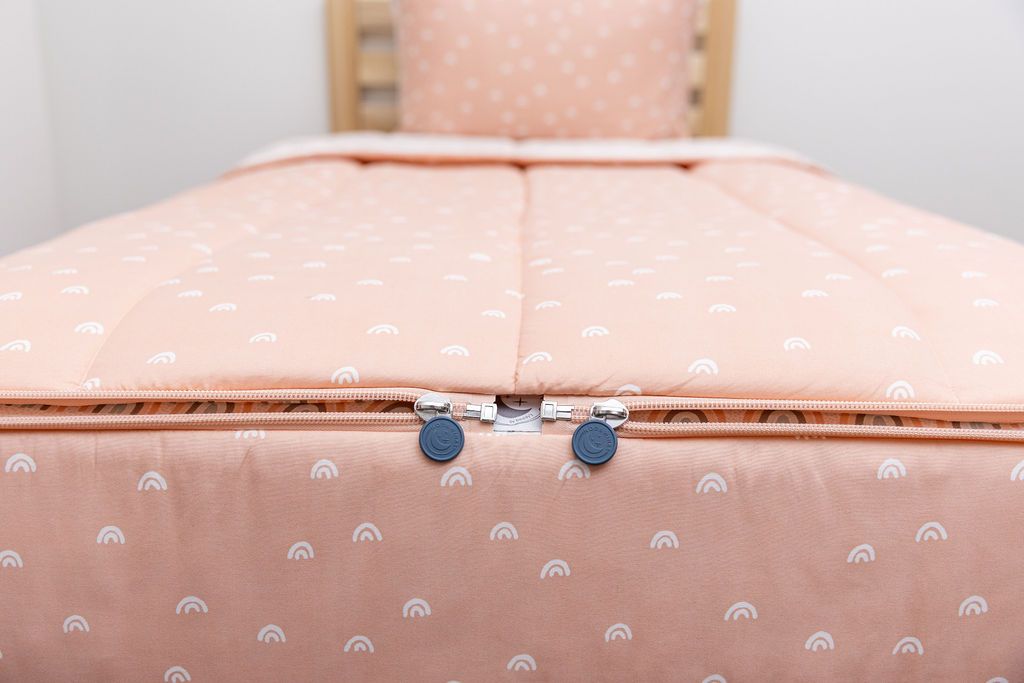 bottom of peachy pink rainbow printed bedding showing two zippers that meet at the end of the bed