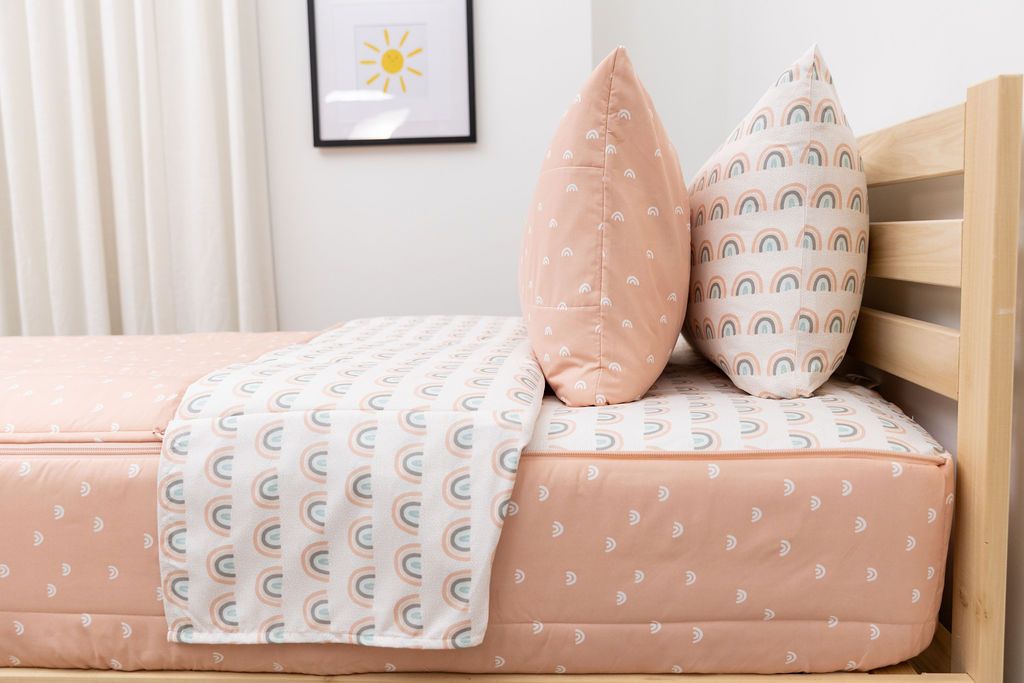 side view of unzipped peachy pink rainbow printed zipper bedding with coordinating pillowcase and sham
