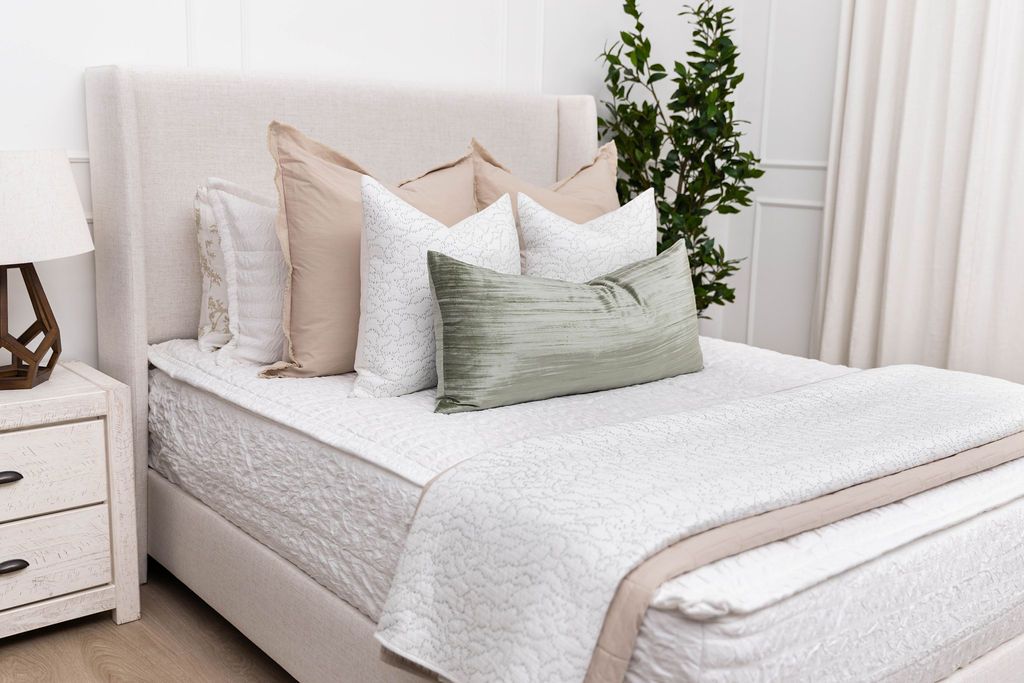A brightly lit bedroom with a bed made with seersucker white zipper bedding and an assortment of neutral pillows and blankets.