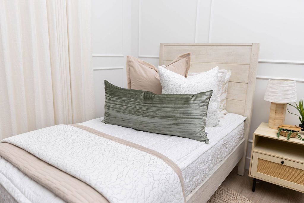 A twin bed made with seersucker white zipper bedding, decorated with neutral and green pillows and throw blankets.