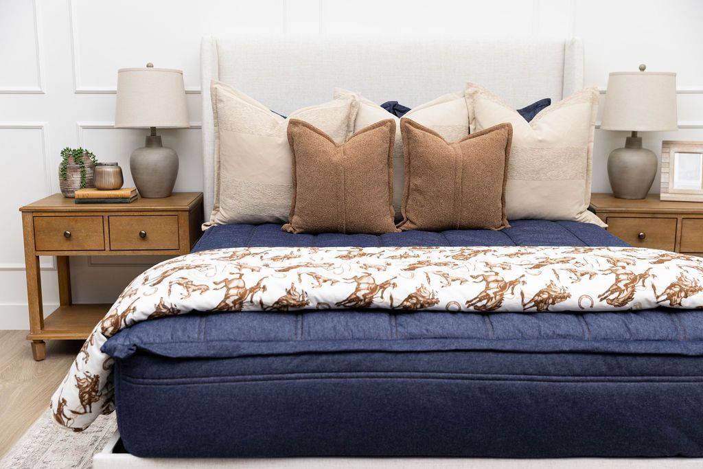A bed made with dark denim blue zipper bedding and an assortment of neutral throw pillows and a cowboy western printed blanket.