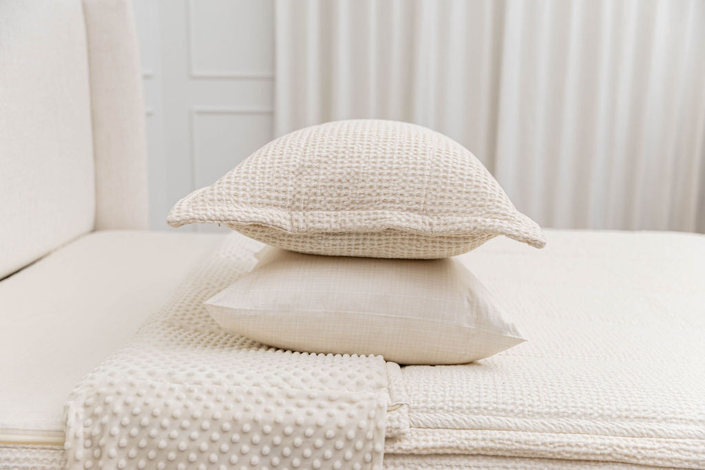 A cream pillowcase and matching sham on a made bed with cream waffle textured zipper bedding.