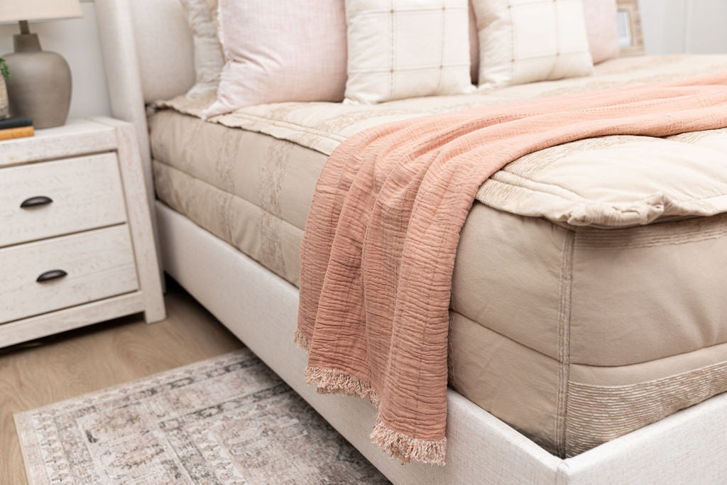 close up shot of a terra cotta pink throw blanket draped across a bed made with tan zipper bedding