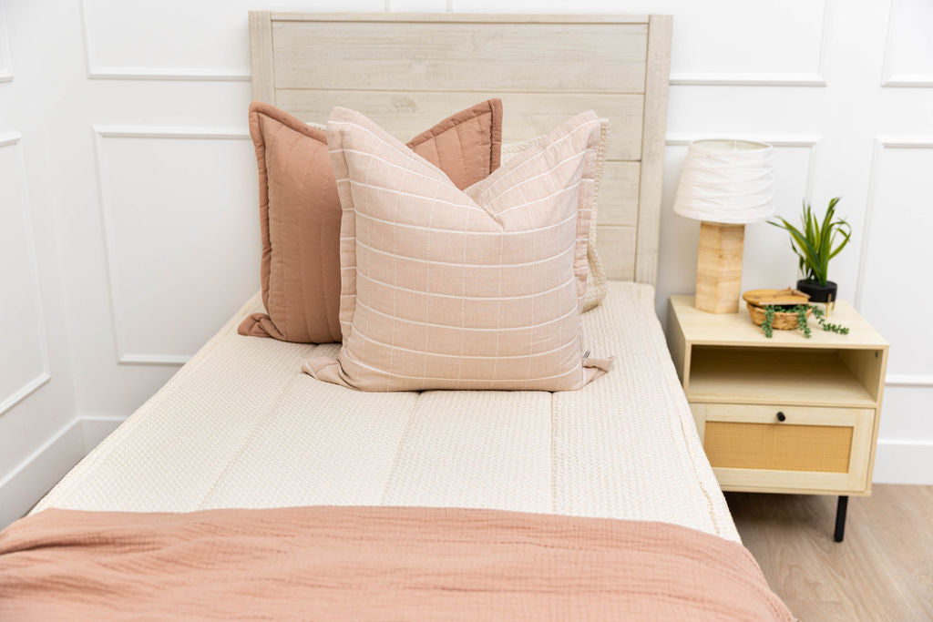 A twin bed made with cream waffle zipper bedding made with pink and terra cotta bedding accessories.