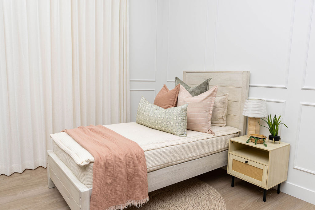 A twin bed made with cream waffle zipper bedding and an assortment of pink and green bedding accessories.