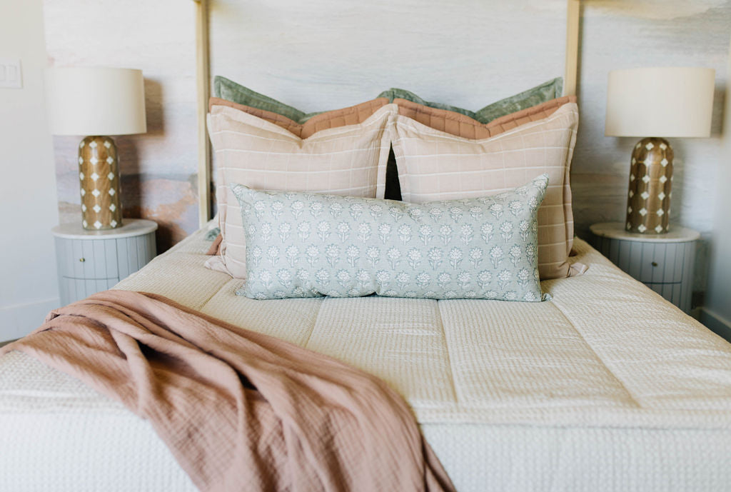 A queen bed made with cream waffle knit zipper bedding with an assortment of pink and green bedding accessories.