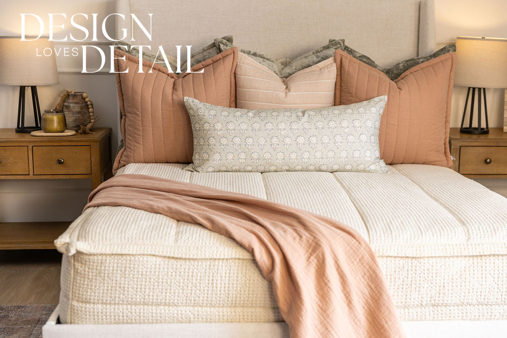 A bed made with cream waffle textured zipper bedding and an assortment of neutral green and pink throw pillows and blanket.