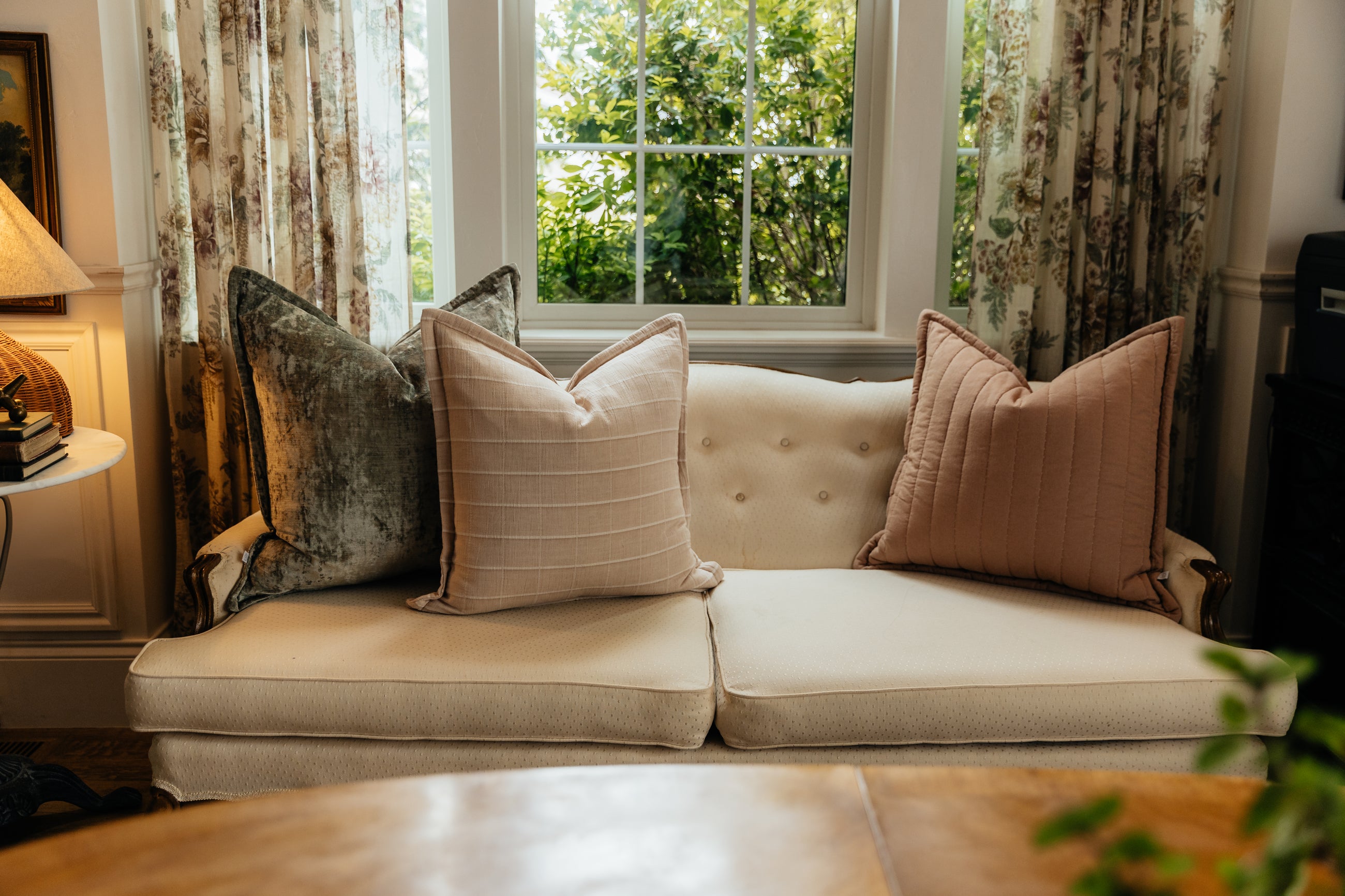 An antique cream couch in a living room with an arrangement of sage green velvet and terracotta pattern pillows.